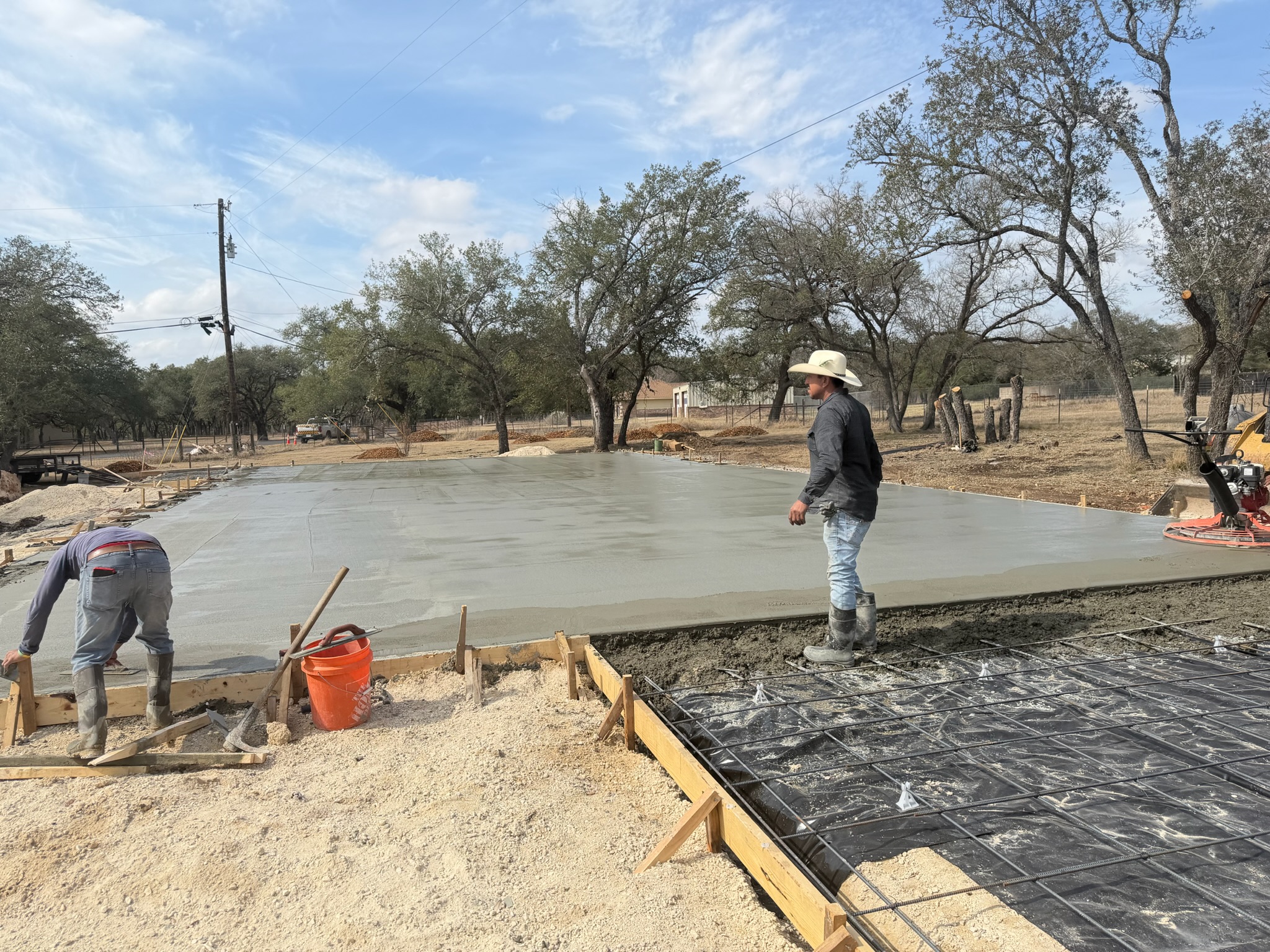 Crew working the edge of a Georgetown TX shop slab with rebar and vapor barrier beside the pour