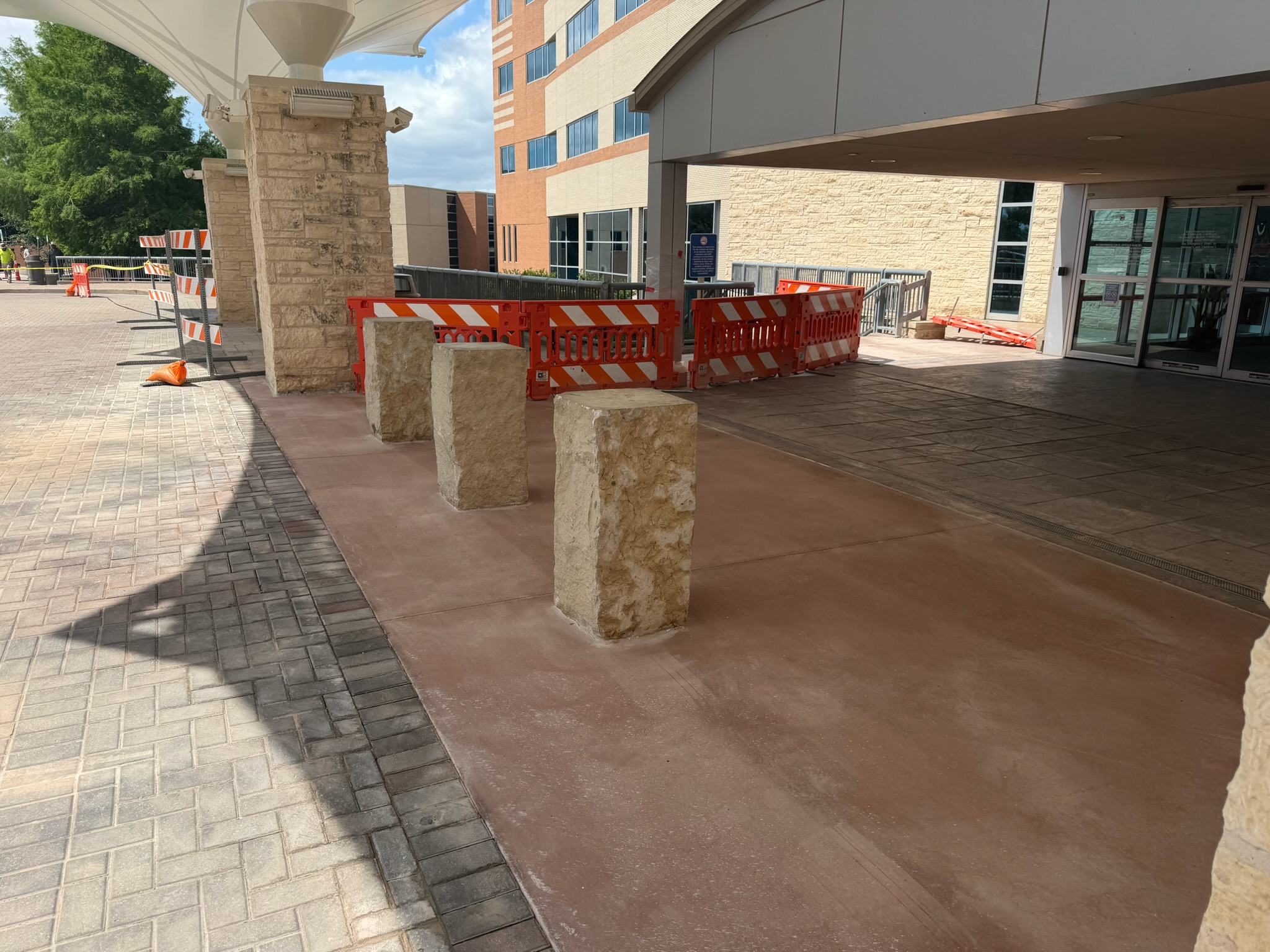 Fresh concrete tied into the covered hospital entry, stone columns, and pedestrian walkway