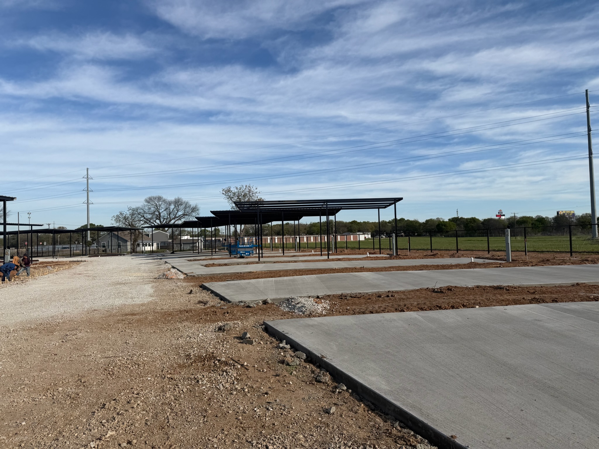 Finished concrete RV pads beside utility posts and covered parking frames