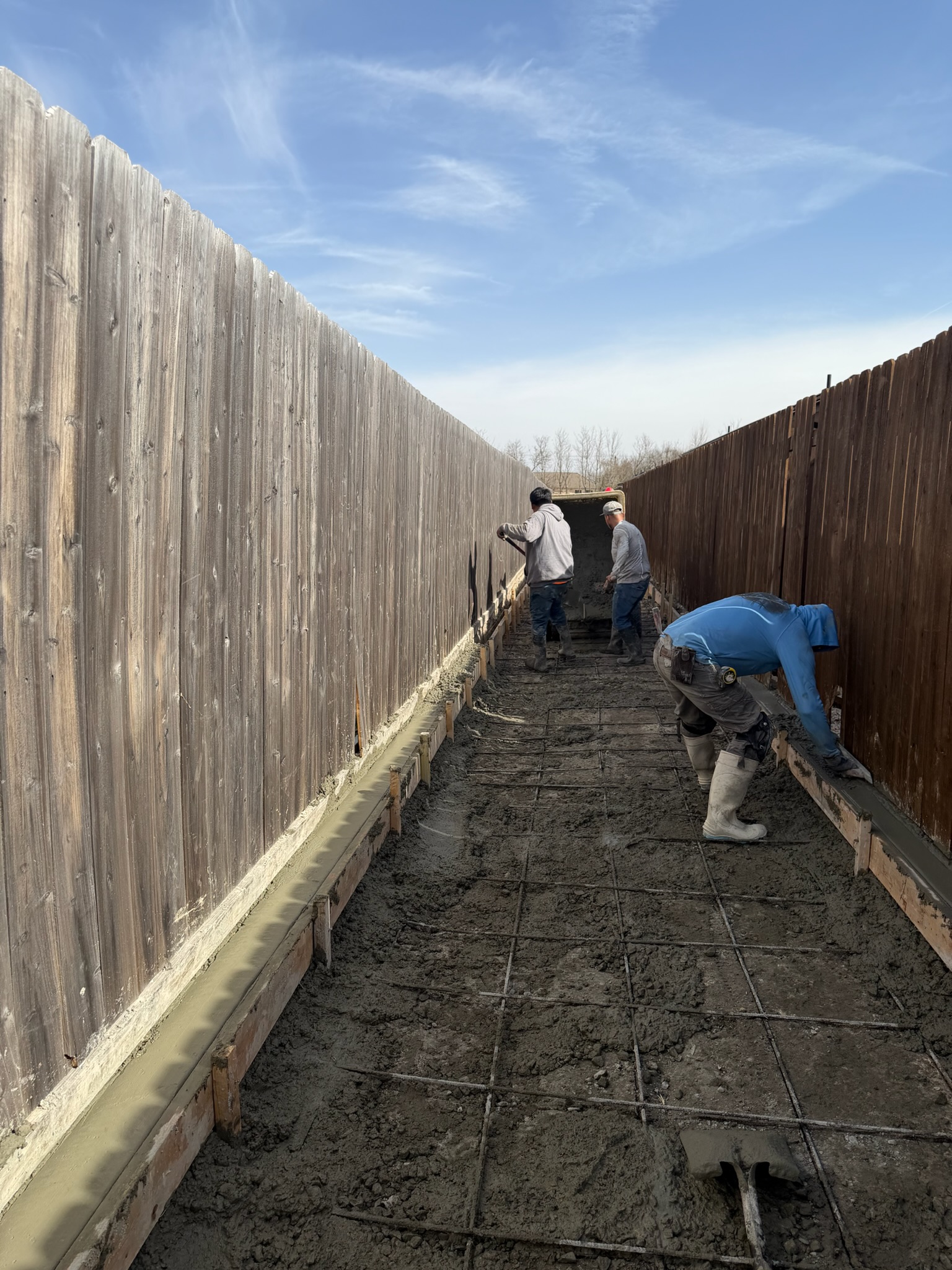 Concrete crew placing and finishing a narrow drainage channel between fences in Temple